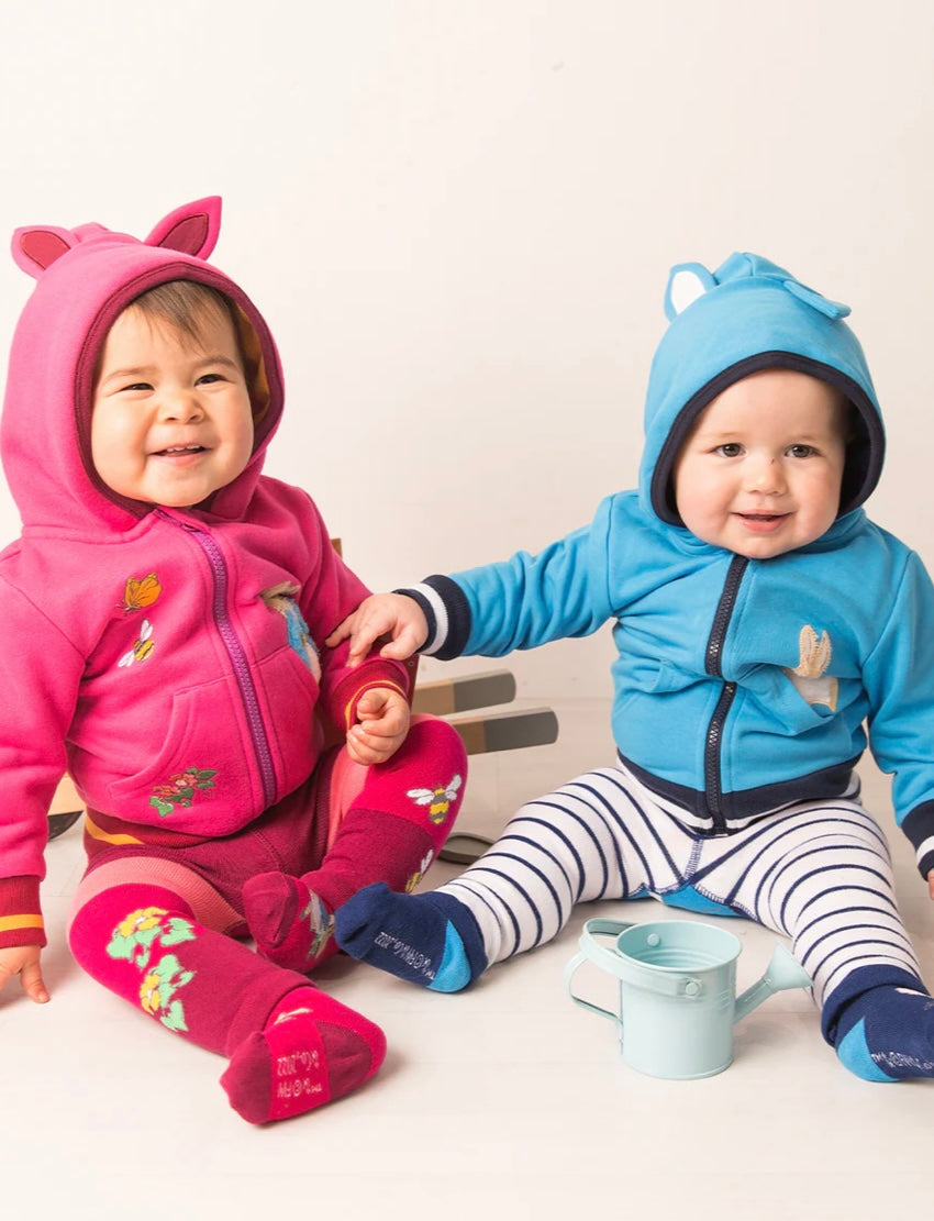 Two children wearing colorful Peter Rabbit hoodies and sitting on a white floor.