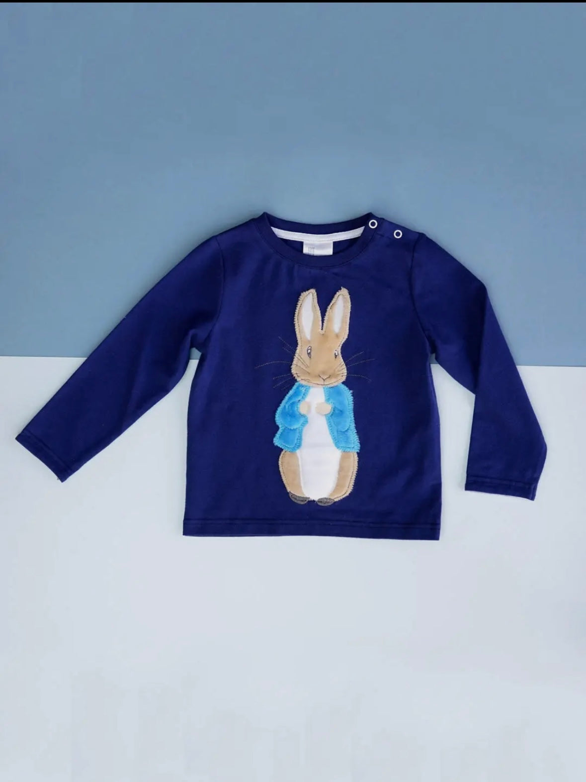 Navy blue long-sleeve shirt with a Peter Rabbit design on a white surface.