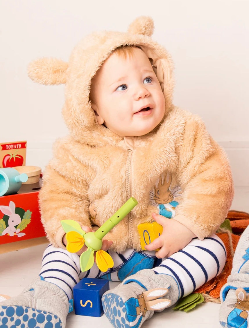 Child in a Peter Rabbit Hoodie holding a toy, surrounded by toys and books on a light background