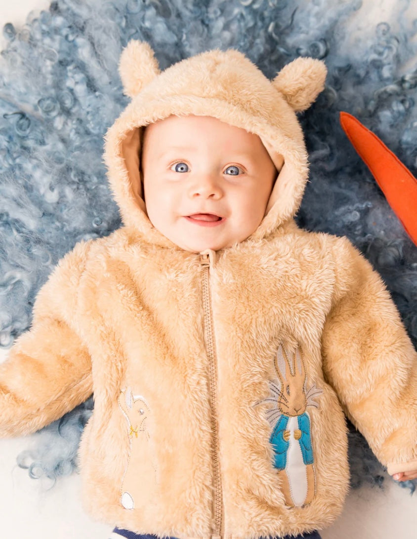 Baby wearing a beige furry Peter Rabbit Hoodie with bear ears on a textured grey background