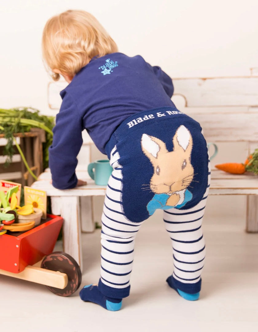 Child wearing a blue outfit with a Peter Rabbit character design, standing in a kitchen.