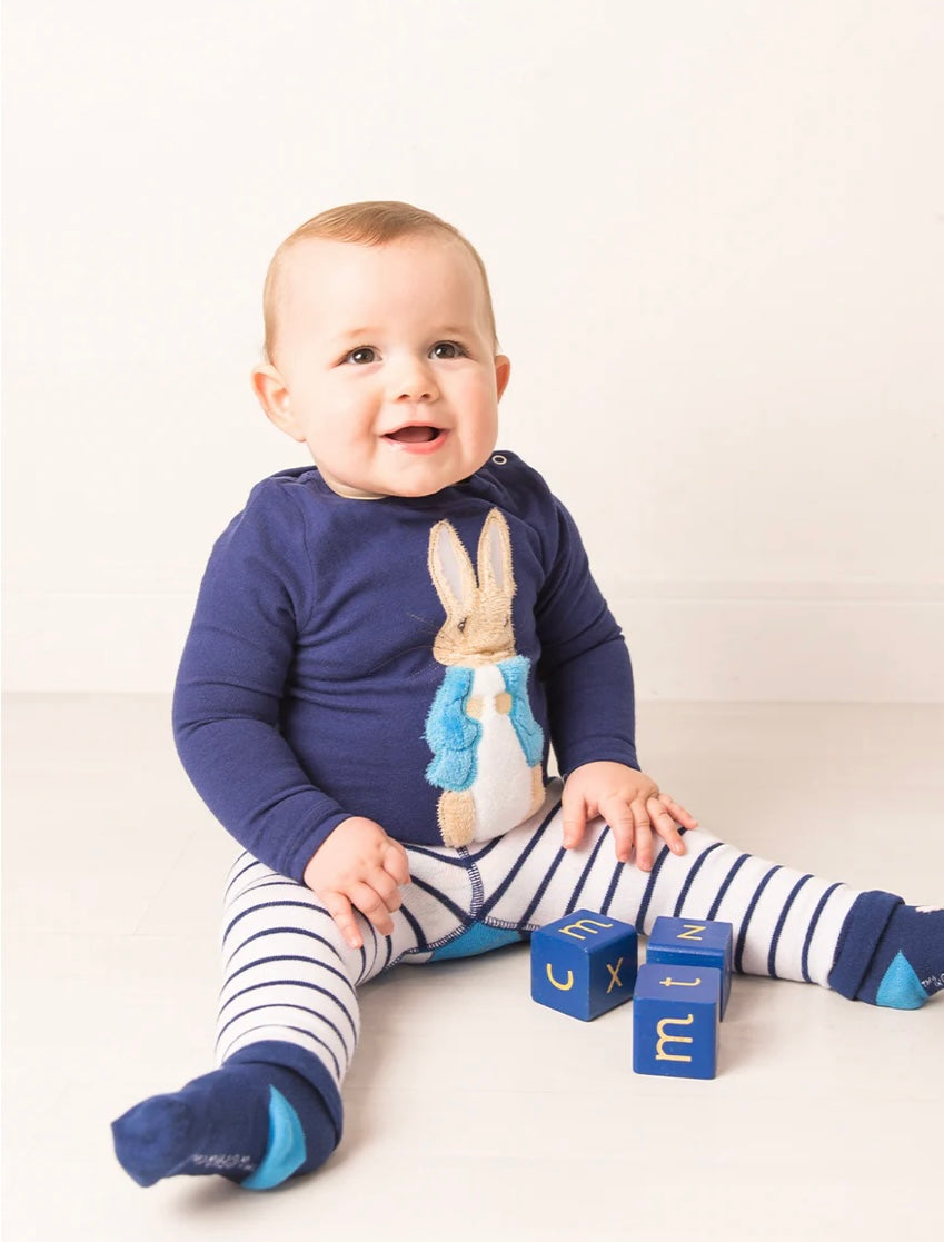 Baby wearing a navy blue outfit with a Peter Rabbit design, sitting on a white surface.